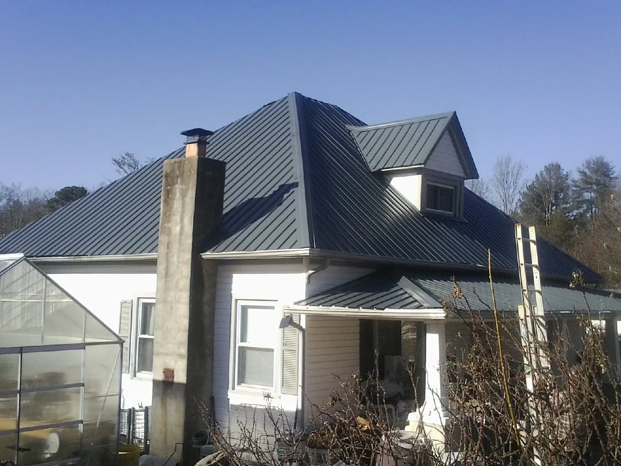 Dark blue standing seam metal roof on a white farmhouse with dormer — Slate & Tile Roof Repair by Roofing Brothers in Kempton