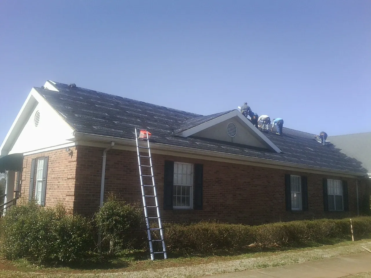 Crew tearing shingles off a brick ranch roof with a ladder set — Metal Roof Repair work by our crew in Kempton